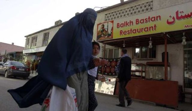 An Afghan woman clad in burqa and her daughter walks past a restaurant built inside part of the only synagogue building in Kabul