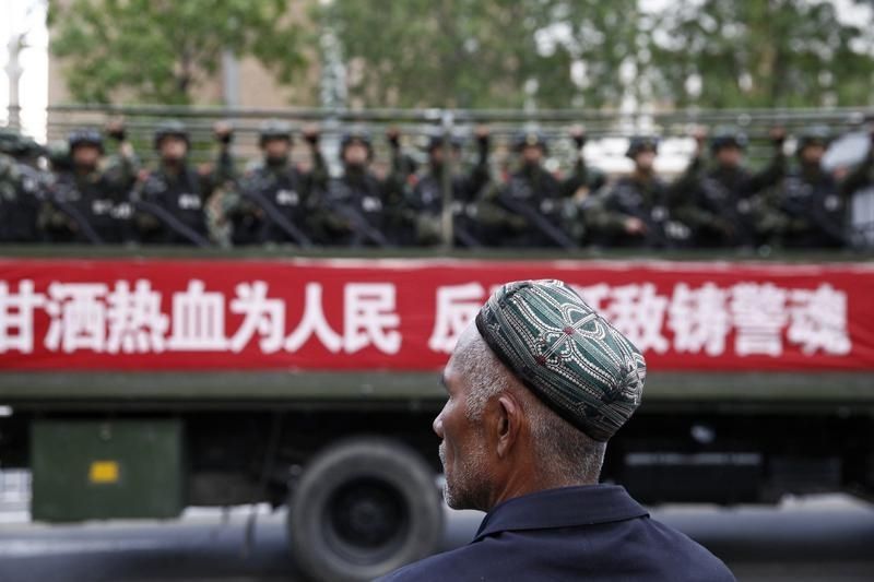 662285-a-uighur-man-looks-on-as-a-truck-carrying-paramilitary-policemen-travel-along-a-street-during-an-ant