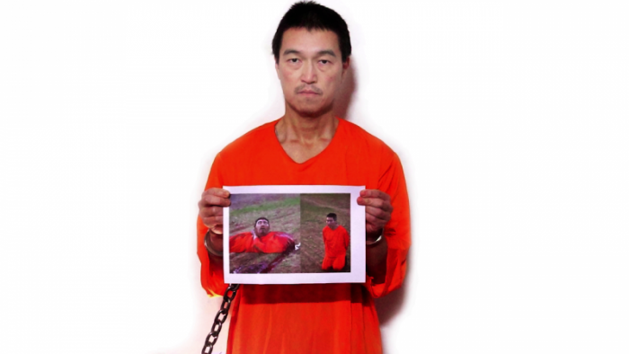 Kenji Goto holding up photo of a beheaded Haruna Yukawa